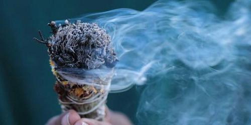 A hand holding a bundle of burning sage.